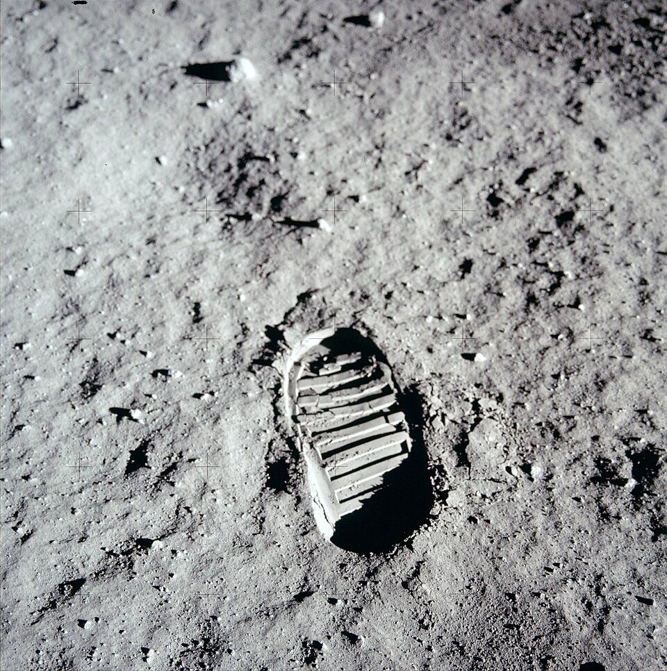 A single bootprint with a ridged tread pressed into fine gray lunar dust.