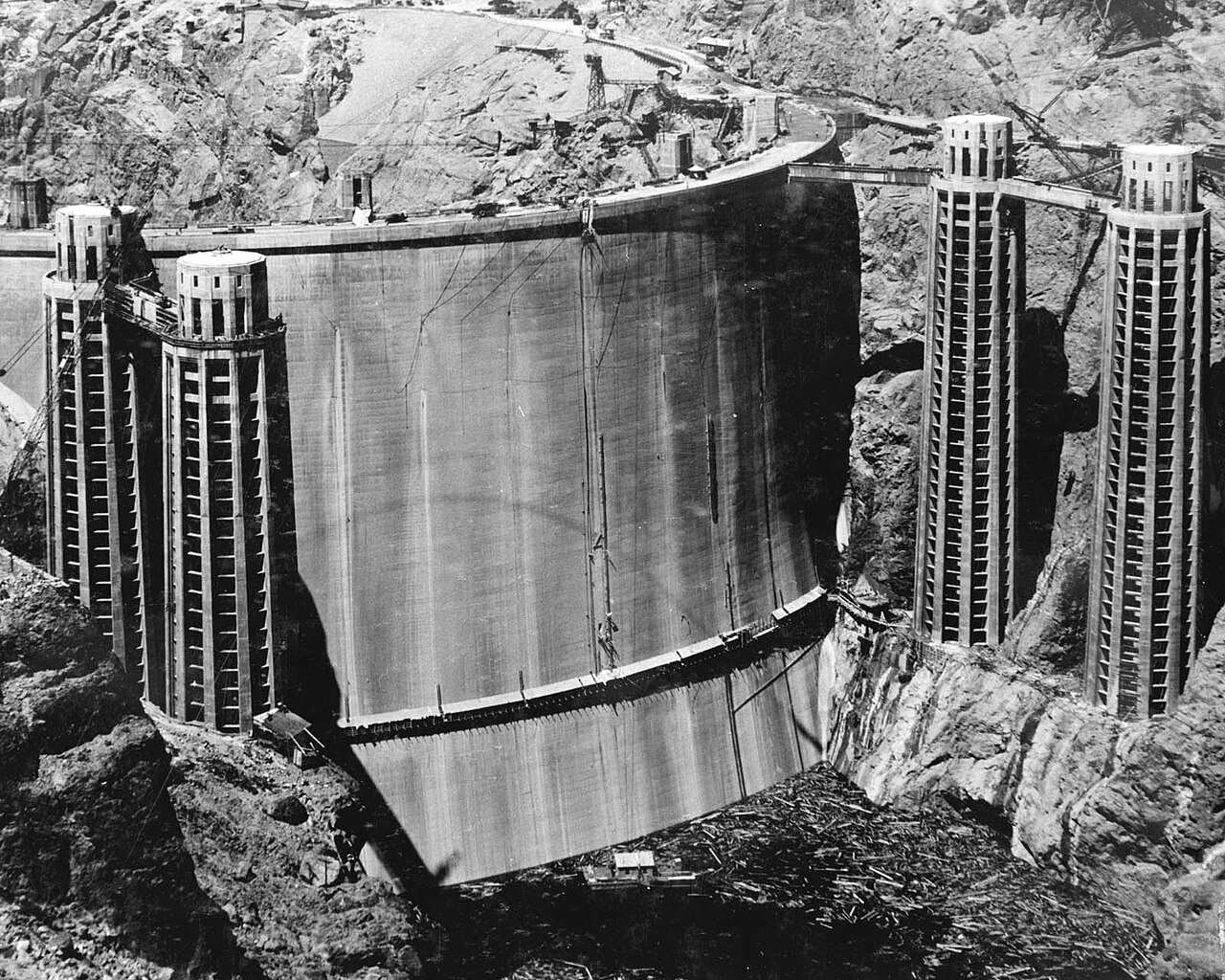 The curved upstream face of Hoover Dam with intake towers at both ends, seen from below in the canyon.