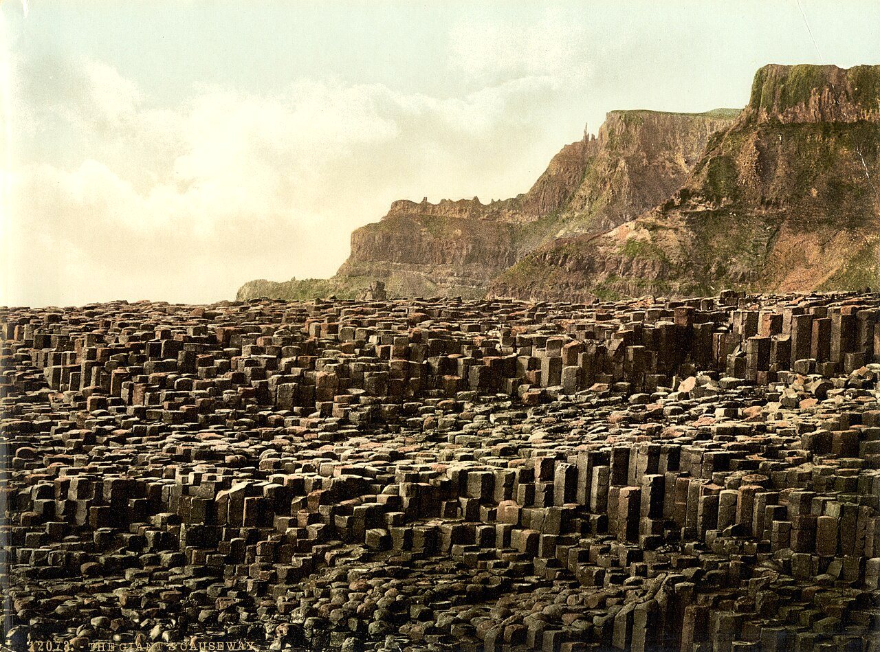 Rows of hexagonal stone columns step down toward the sea beneath a pale sky and a tall headland.