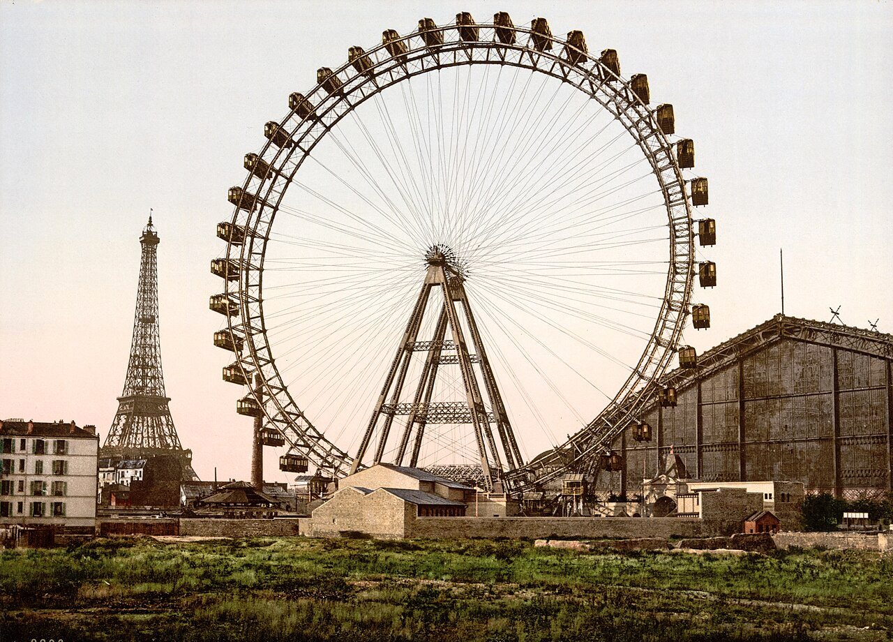 The enormous Grande Roue Ferris wheel stands above a field in Paris, with the Eiffel Tower small on the left.